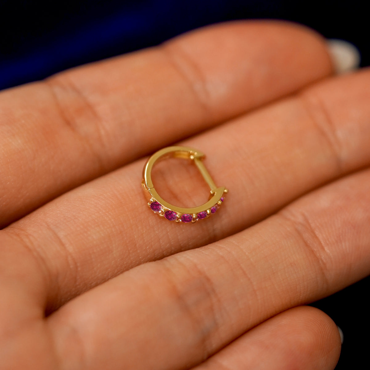 A small Ruby huggie hoop earring on a models fingers