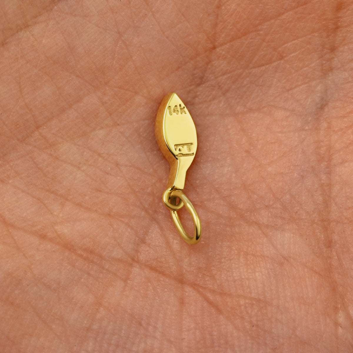 Back view of a solid 14k yellow gold Leaf Charm resting on in the palm of a model's hand
