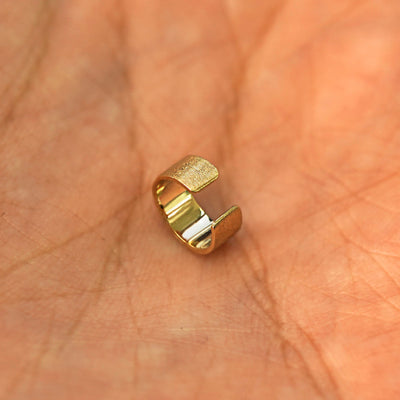 A solid yellow gold Thick Stardust Cuff earring resting in a model's palm on it's side to show the opening of the cuff