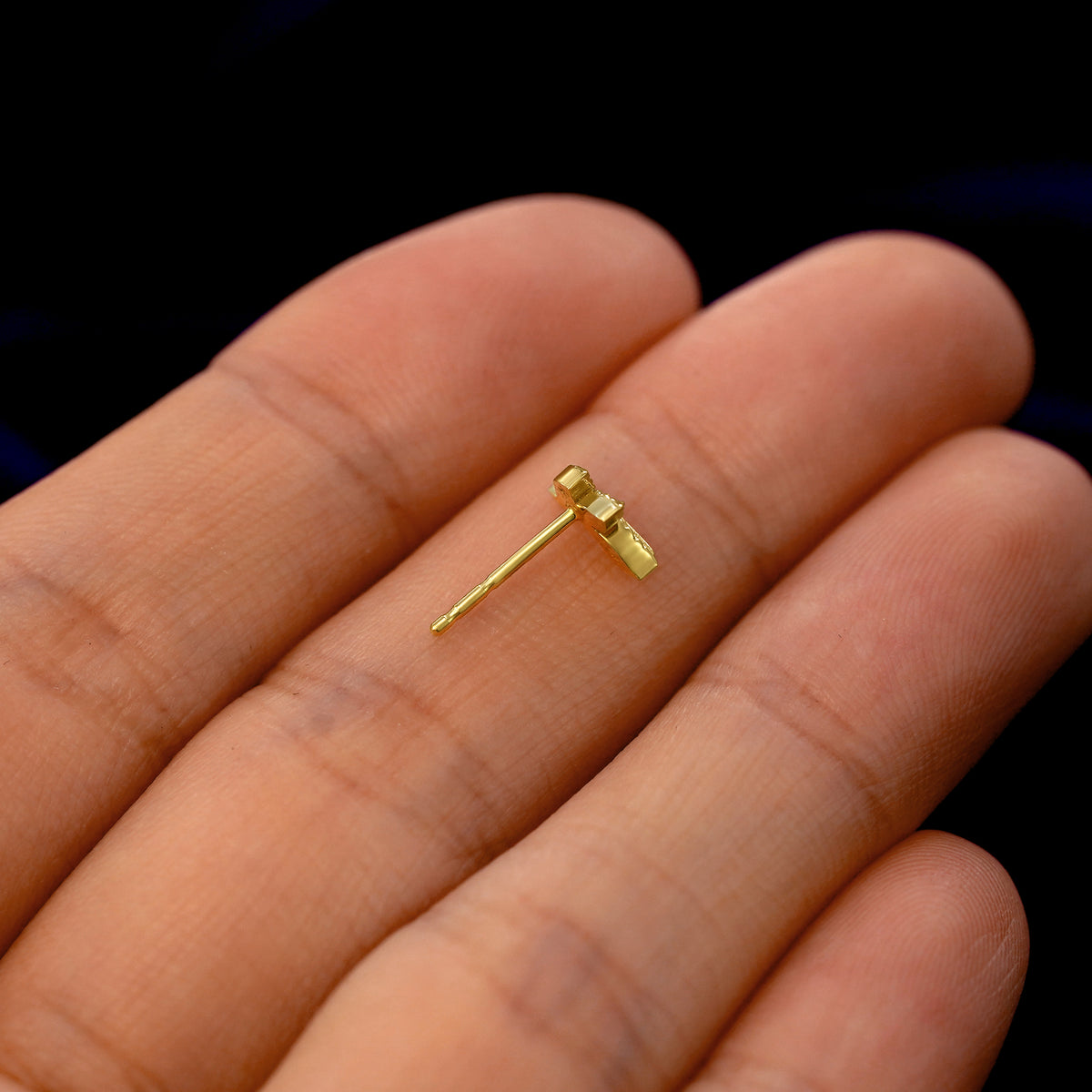 A 14k gold 3 Leaves Earring in a model's hand resting on its side to show the thickness of the earring 