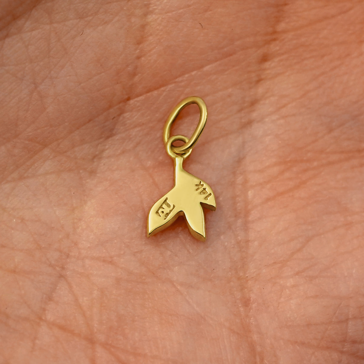 Back view of a solid 14k yellow gold 3 Leaves Charm resting on in the palm of a model's hand