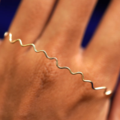 A solid gold Wave Bangle Bracelet resting on the back of a model's hand