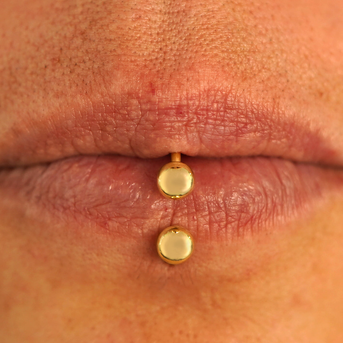 Close up view of a model's lips wearing a 14k yellow gold Medium Horseshoe as a lip ring in their labret