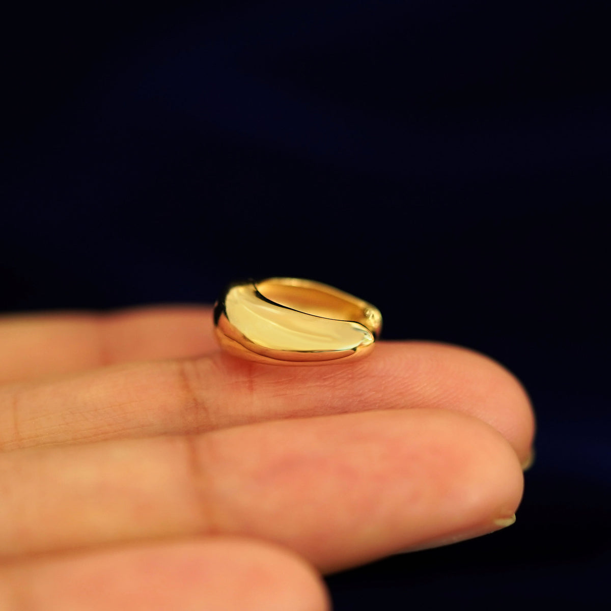 A 14 karat gold Medium Teardrop Huggie Hoop laying on a model's fingertips on it's side