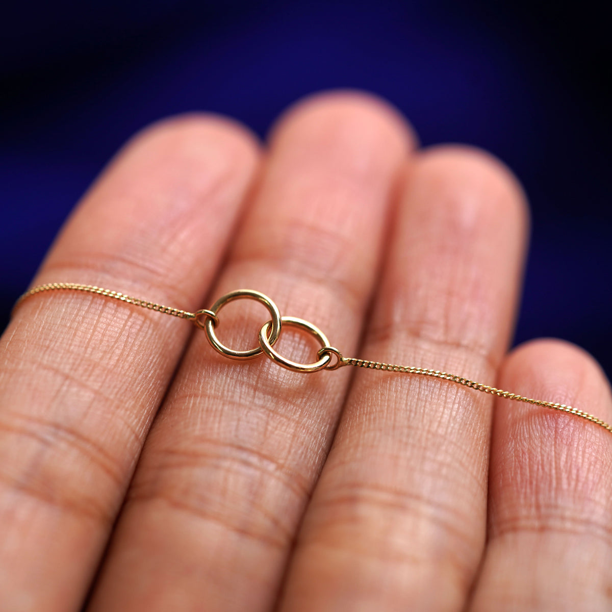 A yellow gold Mini Bound Together Necklace resting on a model's fingers