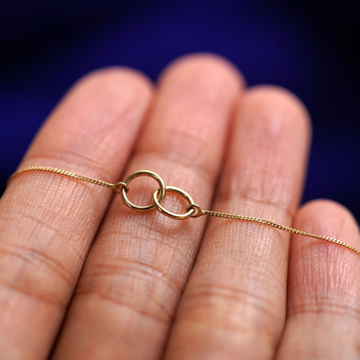 A yellow gold Mini Bound Together Necklace resting on a model's fingers