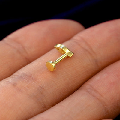 A 14k gold Mini Leaf Flatback Piercing  on a model's fingers resting on its side to show the entire flatback backing