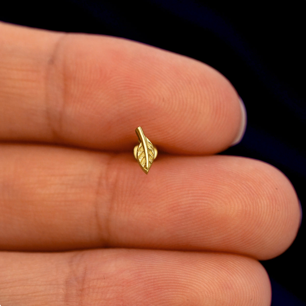 A model holding a solid gold Mini Leaf Flatback Piercing stud  between two fingers
