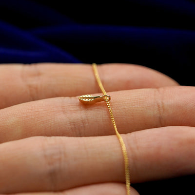 Front side view of a 14k gold mini leaf pendant necklace lying across a model's fingertips