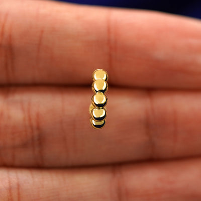 A model's hand holding a yellow gold Mini Puffy Beaded Hoop in between their fingers
