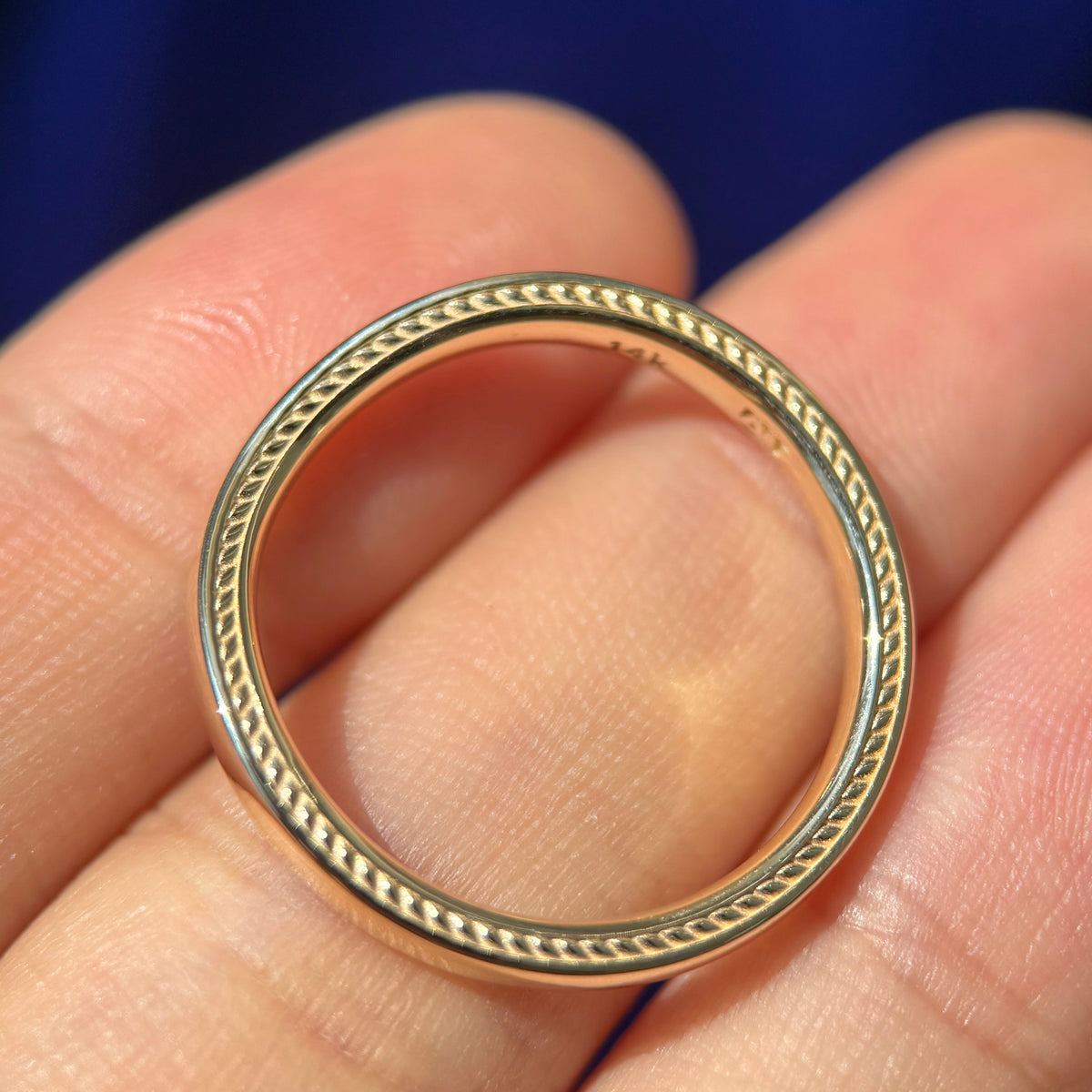14k Yellow Gold 2.8mm Nesting Band with Custom Engravings on sides laying flat in a models hand to show the thickness of  the band