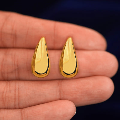 A model's hand holding a pair of 14k yellow gold Teardrop puffy earrings in between their fingers