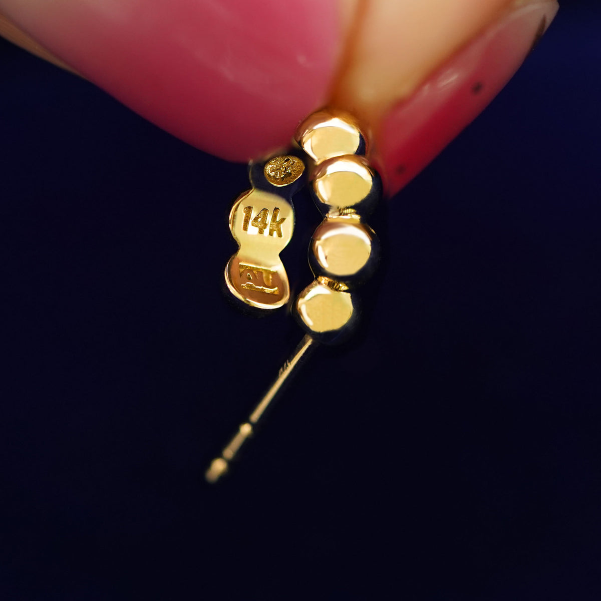 A Mini Puffy Beaded Hoop held between a model's fingers to show the underside view of the hoop
