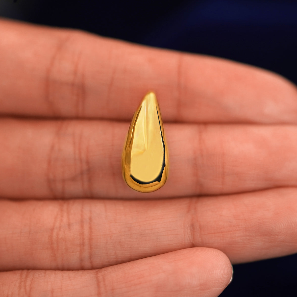 A model's hand holding a yellow gold Teardrop puffy earring in between their fingers