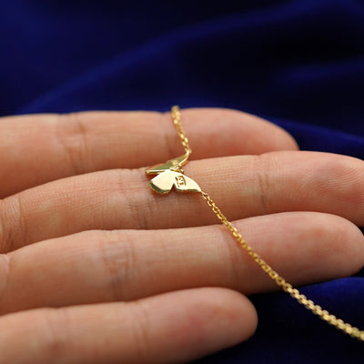 Back side view of a 14k gold butterfly pendant necklace lying across a model's fingertips