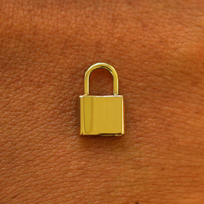A 14 karat solid yellow gold Lock Charm resting on the back of a model's hand