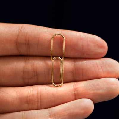 A solid 14k gold Not A Paper Clip Earring resting on a model's fingers