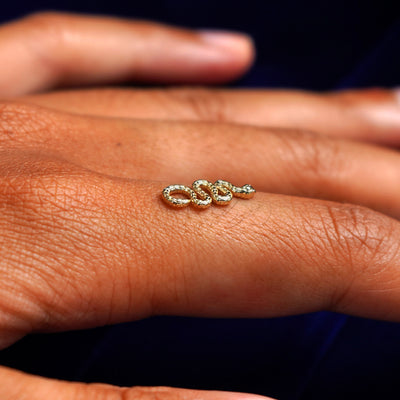 A 14k yellow gold Snake Charm for earring balancing on the back of a model's finger