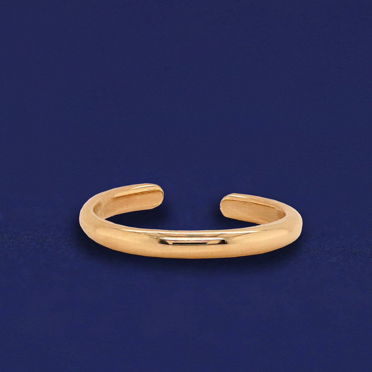 A 14 karat solid yellow gold Single Line Toe Ring on a dark blue background
