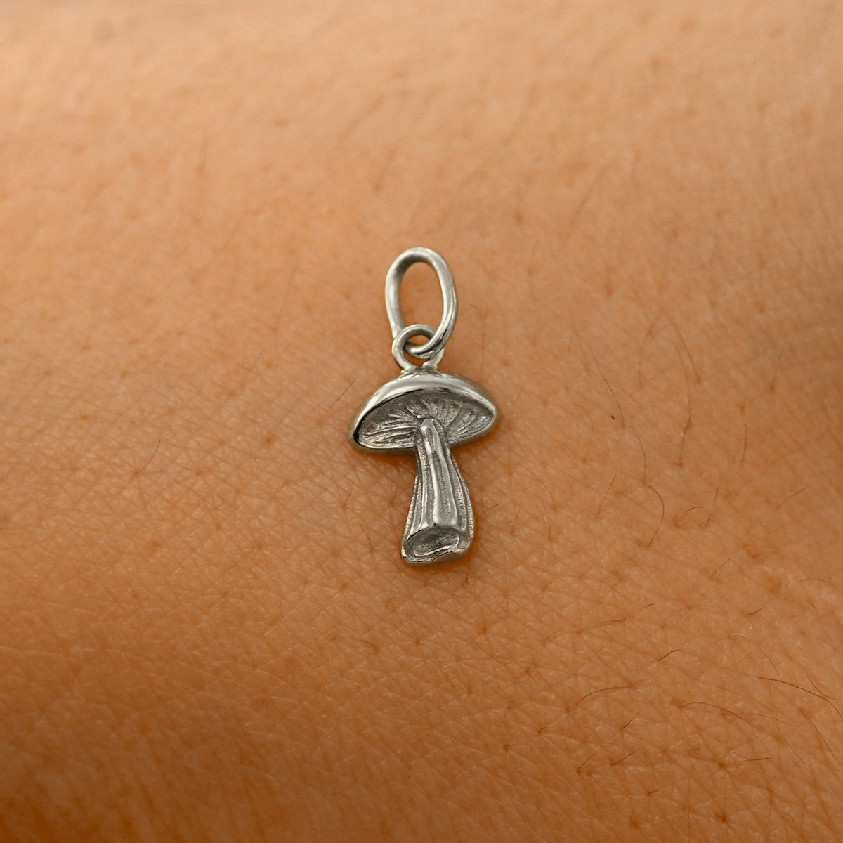 A solid 14k white gold Mushroom Charm resting on the back of a model's hand