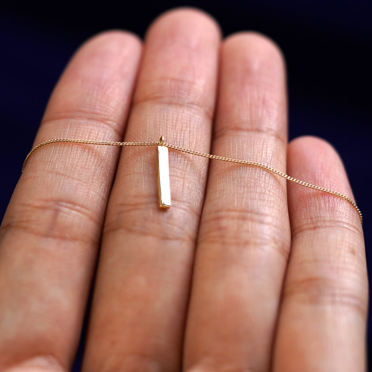 A yellow gold Bar Necklace resting on a model's fingers