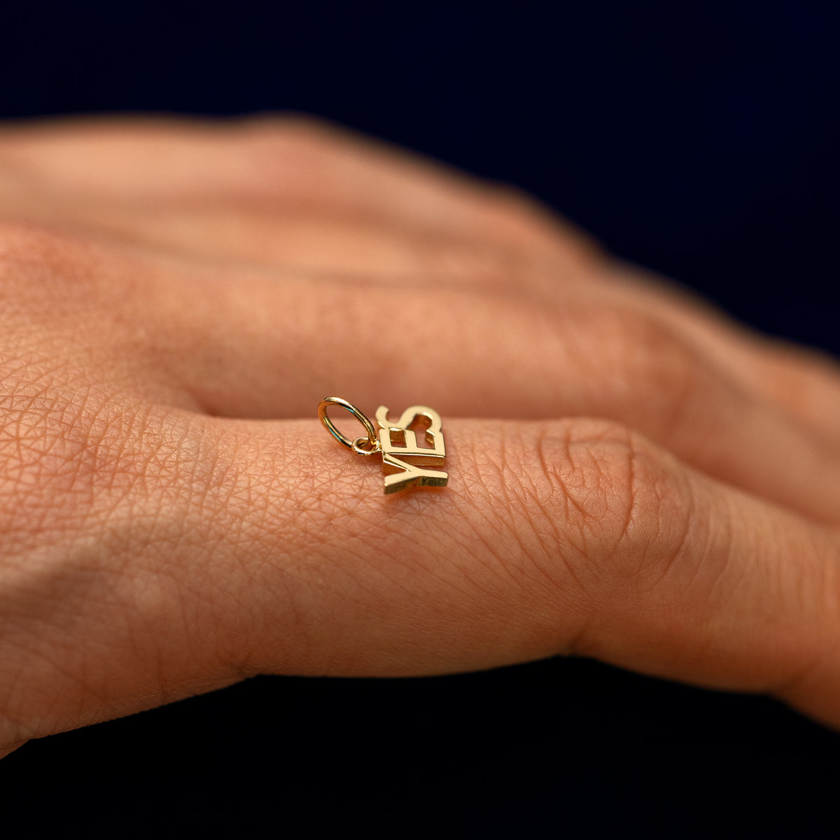 A solid 14k gold Yes charm resting on a models finger to show the bail details