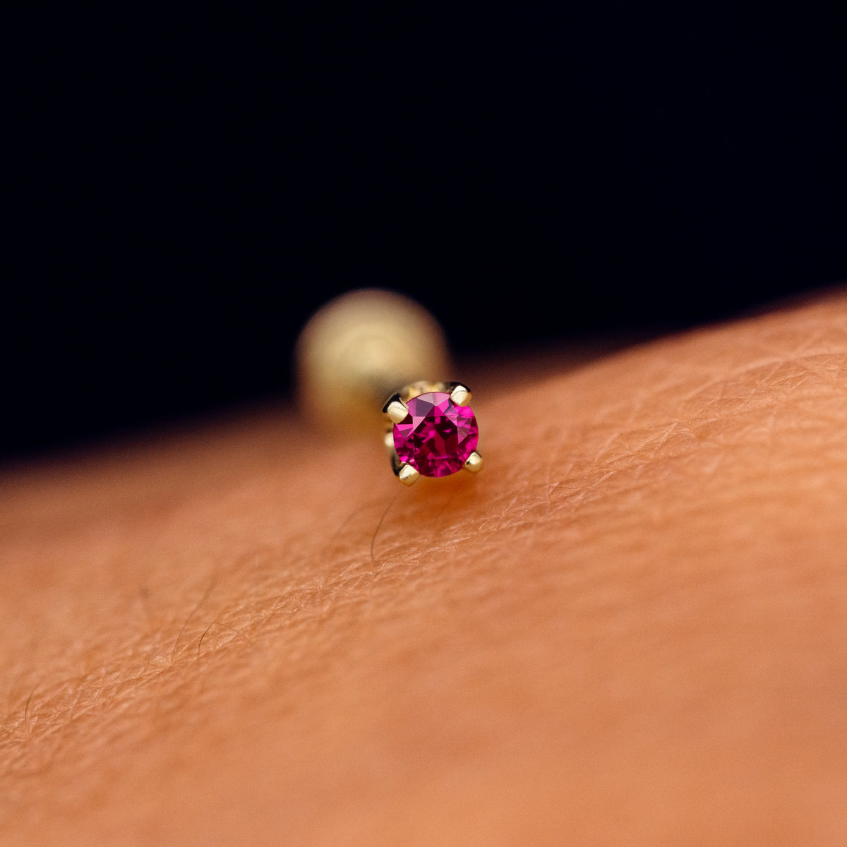 A solid 14k yellow gold 2mm Gemstone Flatback Piercing resting on the back of a model's hand