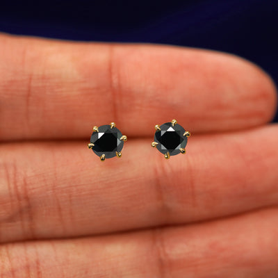 A pair of solid yellow gold black 5mm Moissanite Earrings in between a model's fingers