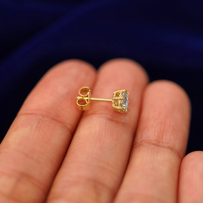 A 14k gold clear 5mm Moissanite Earring sitting sideways on a model's fingertips to show detail