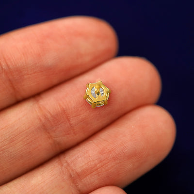 A yellow gold 5mm Moissanite Earring laying facedown on a model's fingers to show the underside view