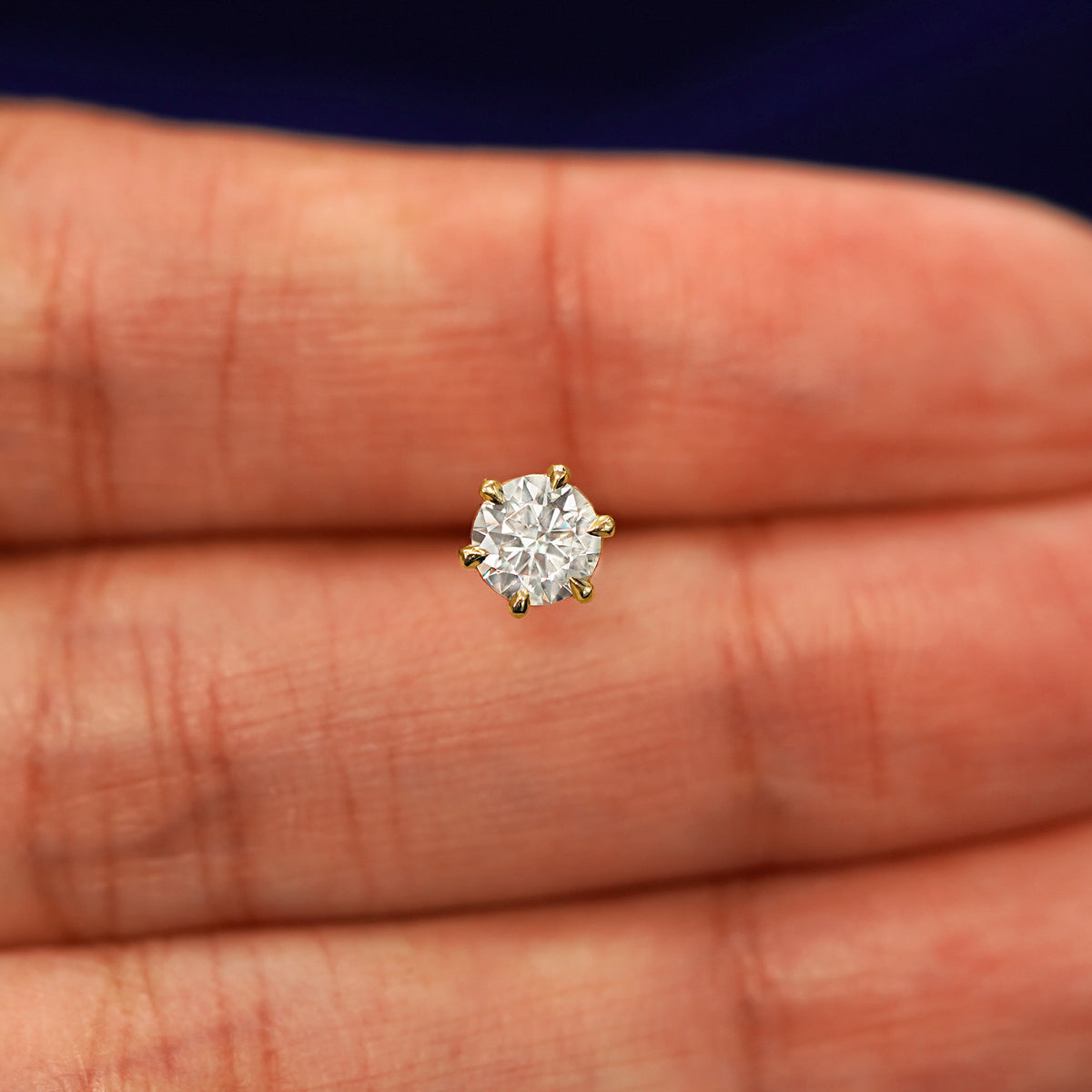 A solid 14k yellow gold clear 5mm Moissanite Earring in between a model's fingers