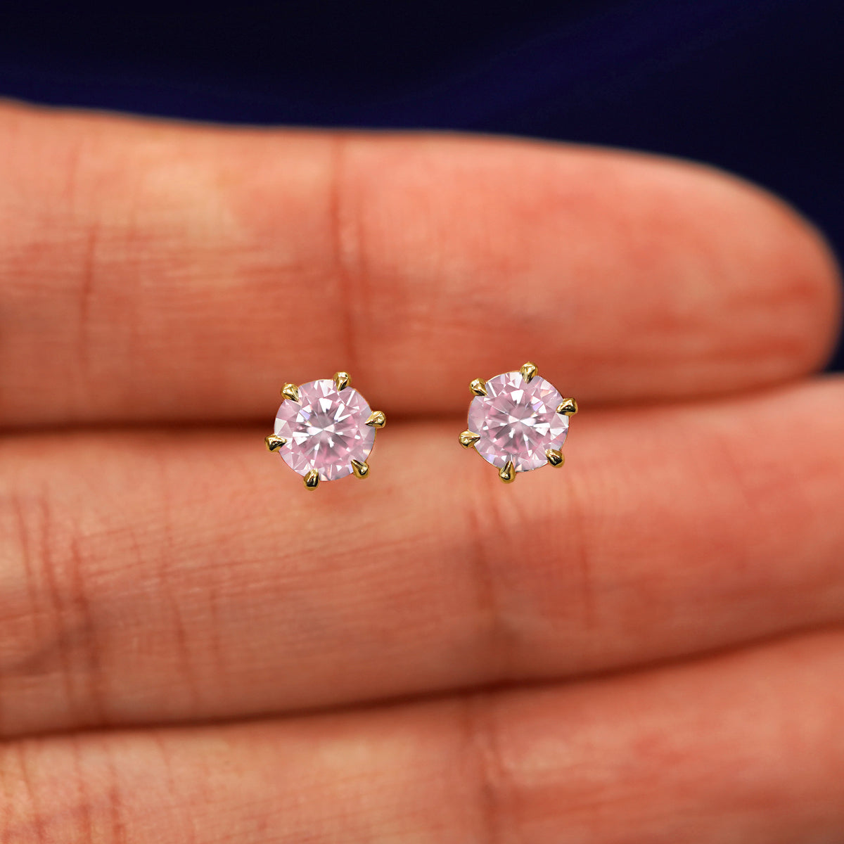 A pair of solid yellow gold pink 5mm Moissanite Earrings in between a model's fingers