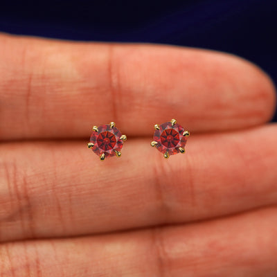 A pair of solid yellow gold red 5mm Moissanite Earrings in between a model's fingers