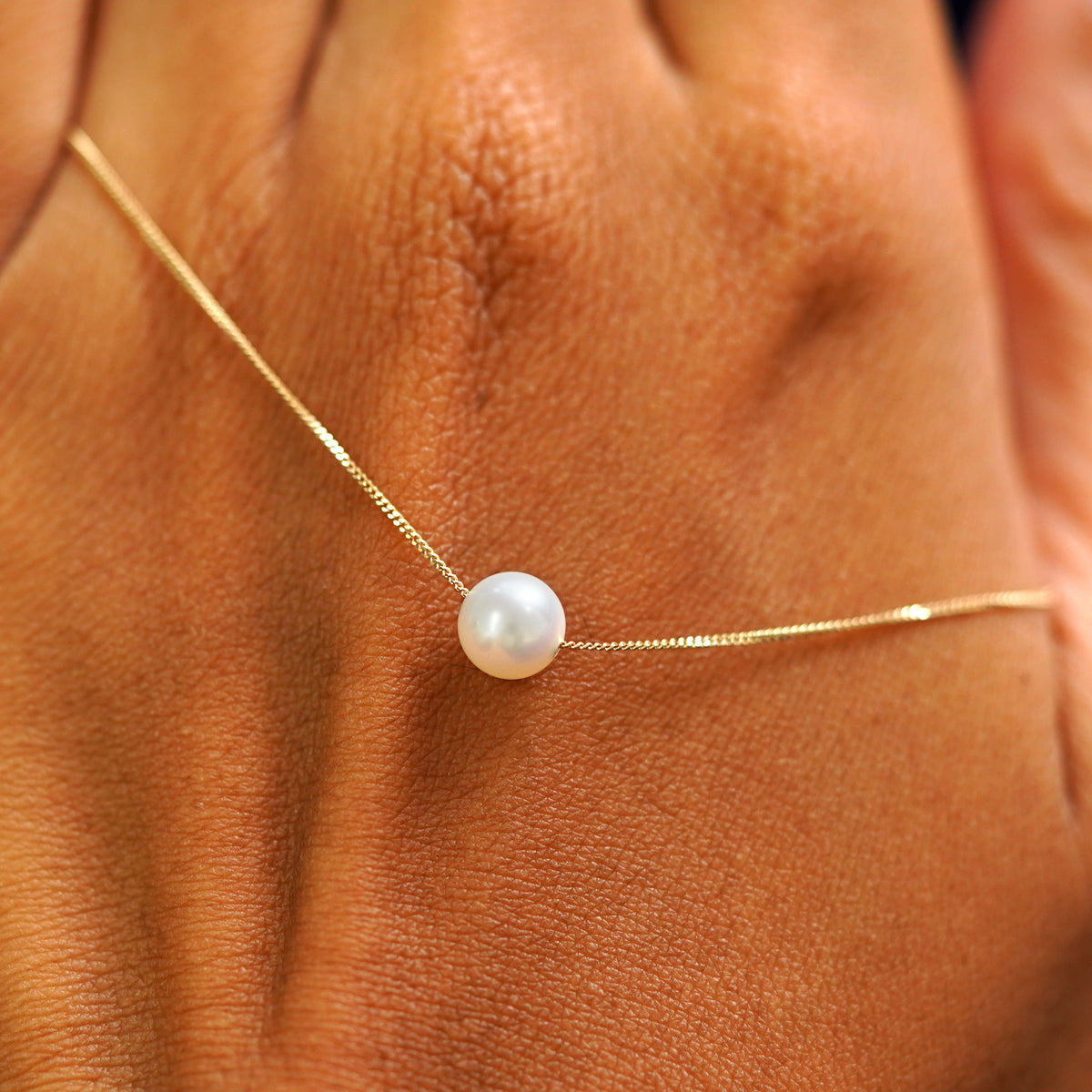 A 6mm pearl slide necklace resting on the back of a model's hand