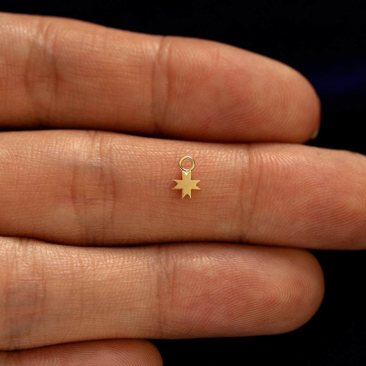 A solid gold 8 Pointed Star Charm for chain resting in a model's palm