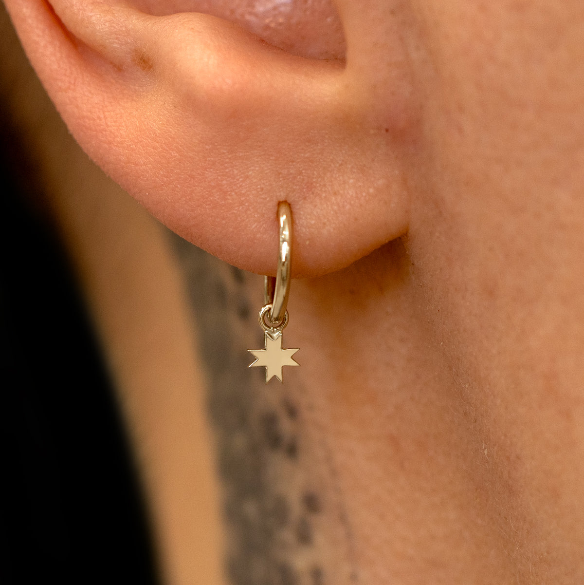 Close up view of a model's ear wearing a champagne gold 8 Pointed Star Charm on a Seamless Huggie Hoop