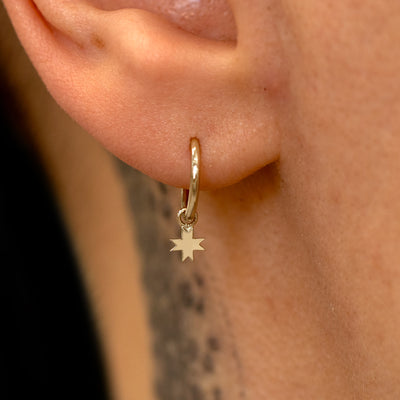 Close up view of a model's ear wearing a champagne gold 8 Pointed Star Charm on a Seamless Huggie Hoop