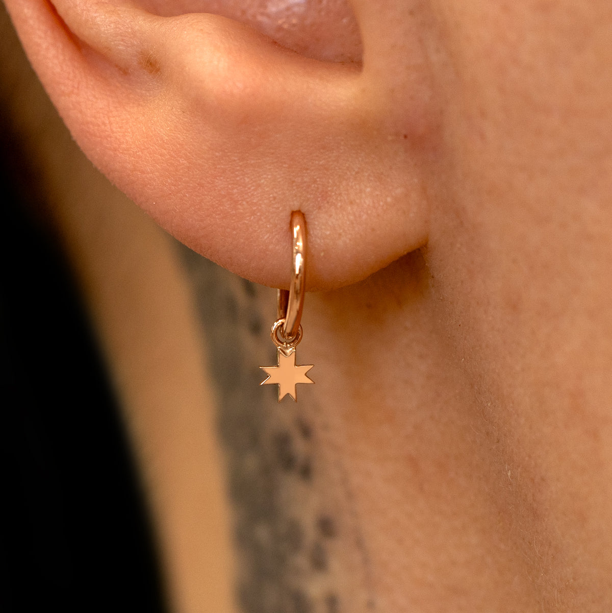 Close up view of a model's ear wearing a rose gold 8 Pointed Star Charm on a Seamless Huggie Hoop