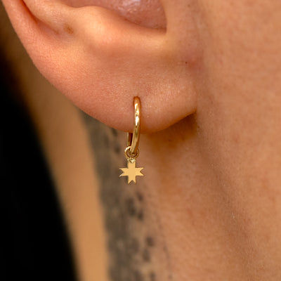 Close up view of a model's ear wearing a yellow gold 8 Pointed Star Charm on a Seamless Huggie Hoop