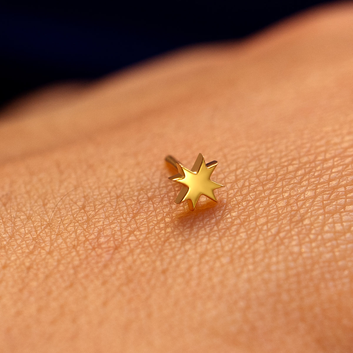 Close up view of the face of an 8 pointed star flatback piercing on the back of a models hand