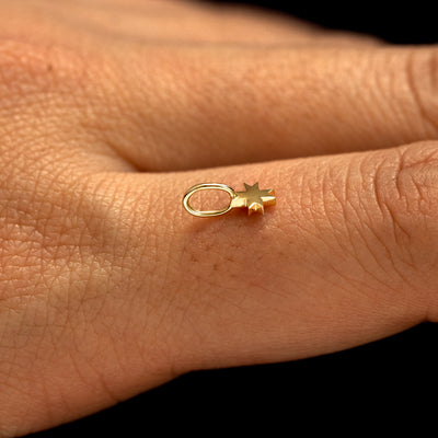 A 14k yellow gold 8 Pointed Star Charm for chain balancing on the back of a model's finger