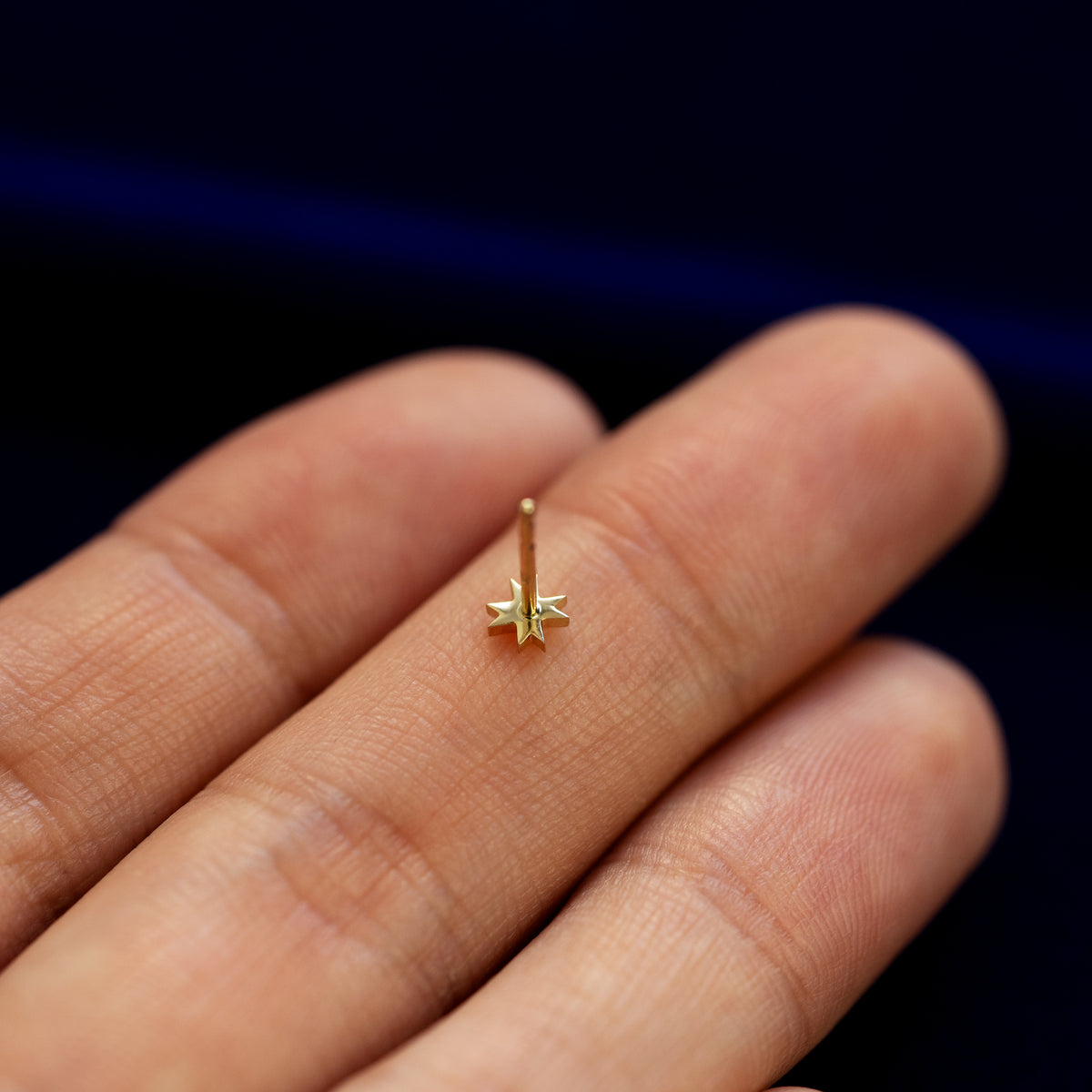 An 8 pointed star stud earring with no backing laying face down on a models fingers to show the back of the stud