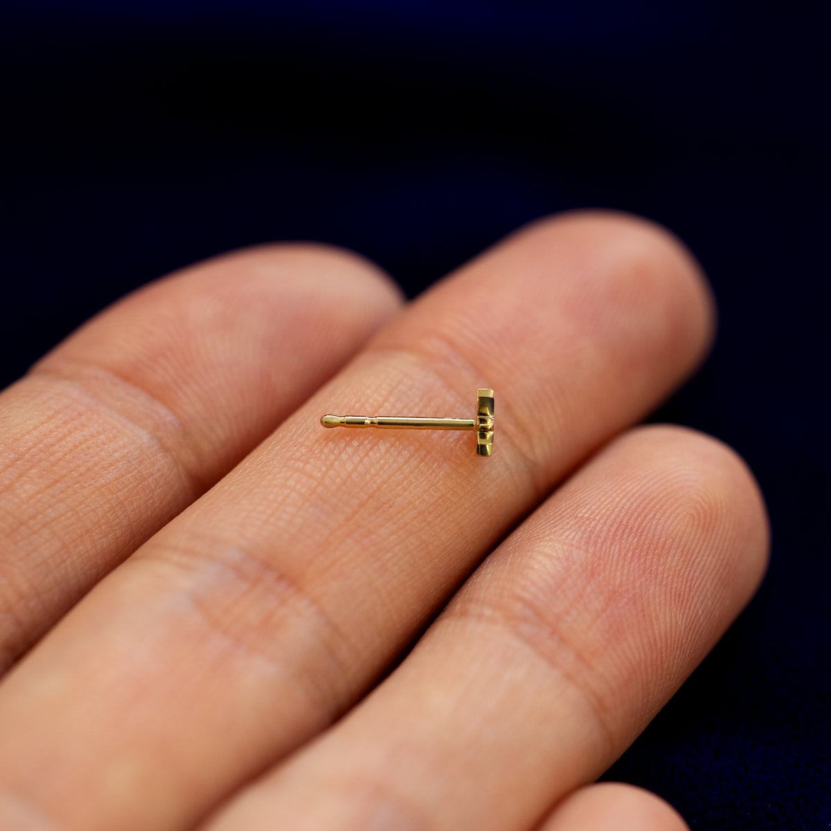 An 8 pointed star stud earring with no backing laying sideways on a models fingers to show the thickness of the stud