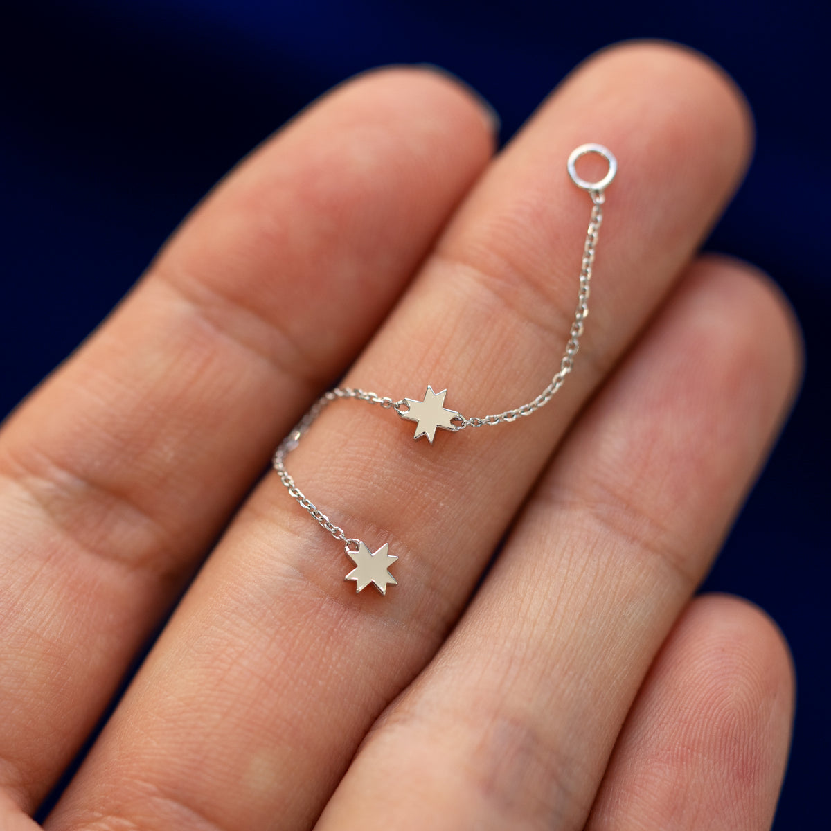 An 8 pointed star extender earring curled up in a models hand to show the connecting ring and the flexibility of the chain