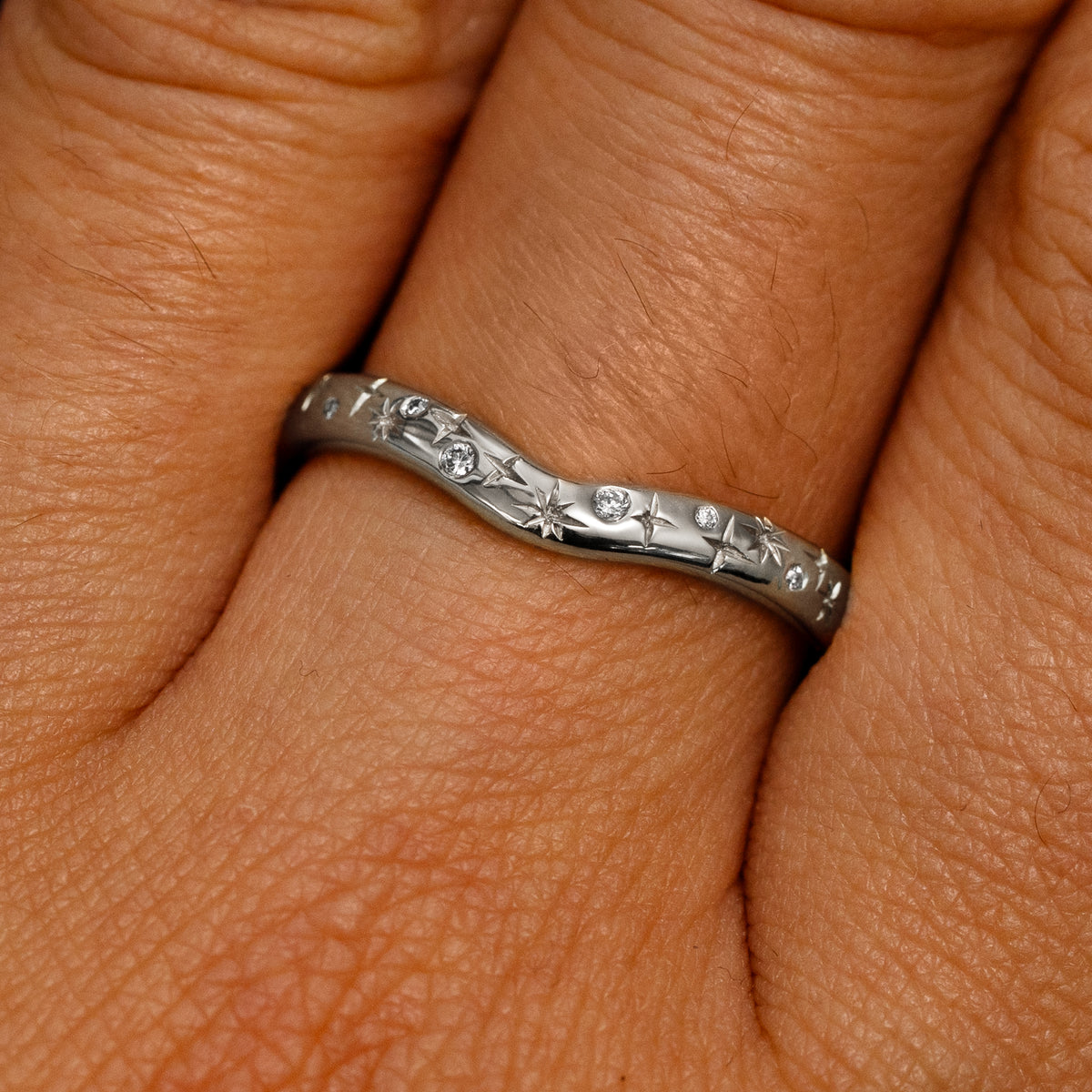 Close up view of a model's fingers wearing a 950 platinum Curvy Chevron Diamond Stars Band