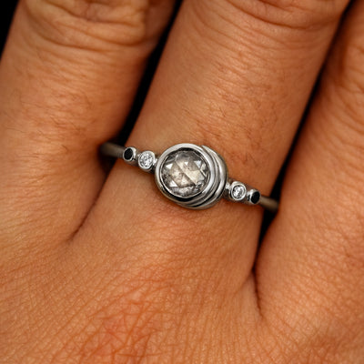 A model's hand wearing a 950 platinum Rose Cut Salt and Pepper Diamond Moon Ring