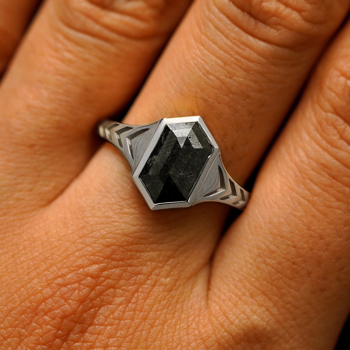 Close up view of a model's fingers wearing a 950 platinum elongated hexagon black diamond engraved chronos ring