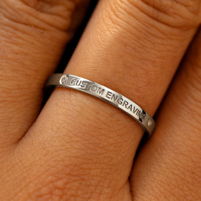 A model's finger wearing a diamond 950 platinum flush gemstone industrial band the words custom engraving on the top