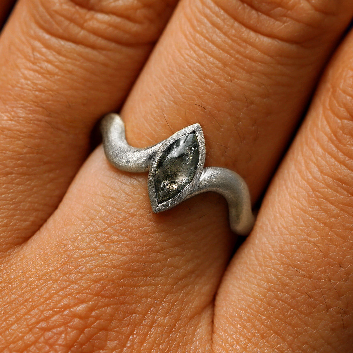 Close up view of a model's hand wearing a 950 platinum marquise cabochon salt and pepper diamond engagement ring