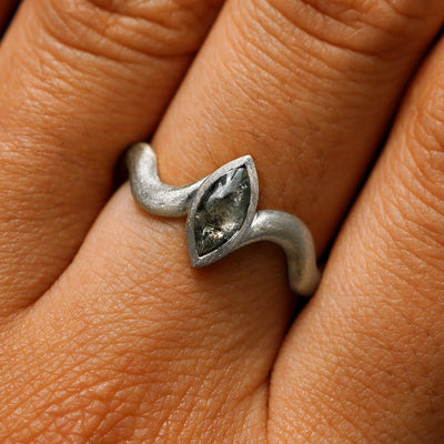 Close up view of a model's hand wearing a 950 platinum marquise cabochon salt and pepper diamond engagement ring